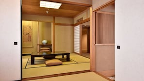 A traditional Japanese room with tatami flooring, a low table, cushions, and sliding doors.