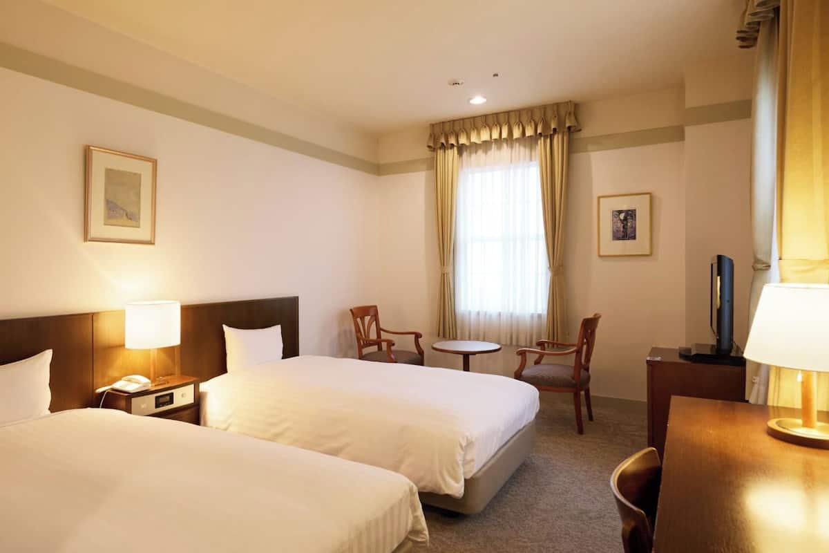 Ett hotellrum med två sängar, ett skrivbord, en stol, ett litet bord och en tv.