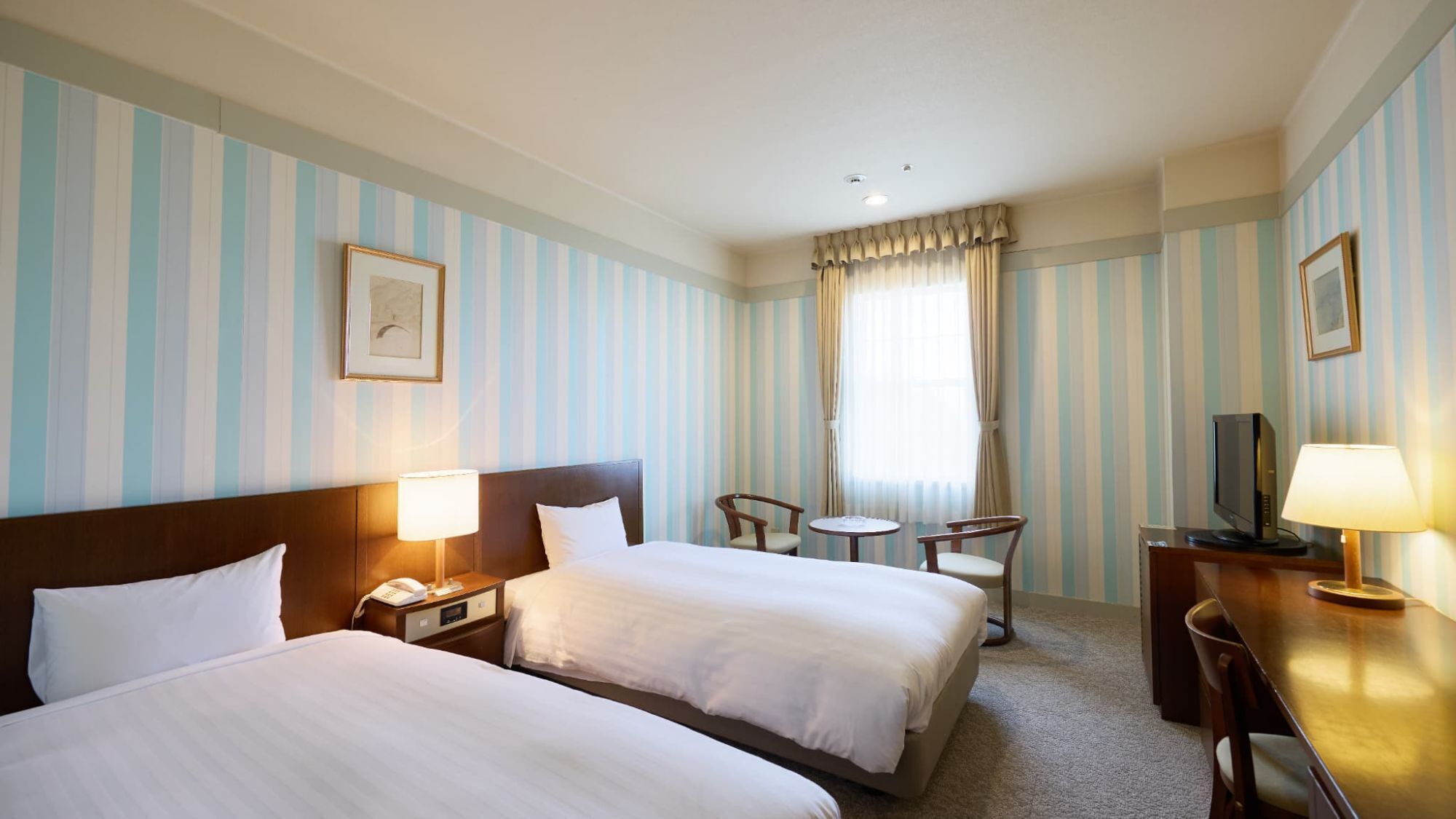 Ein Hotelzimmer mit zwei Betten, einem Schreibtisch mit Fernseher, einem kleinen Tisch und einem Stuhl.