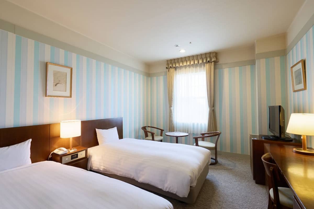 Ein Hotelzimmer mit zwei Betten, einem Schreibtisch mit Fernseher, einem kleinen Tisch und einem Stuhl.