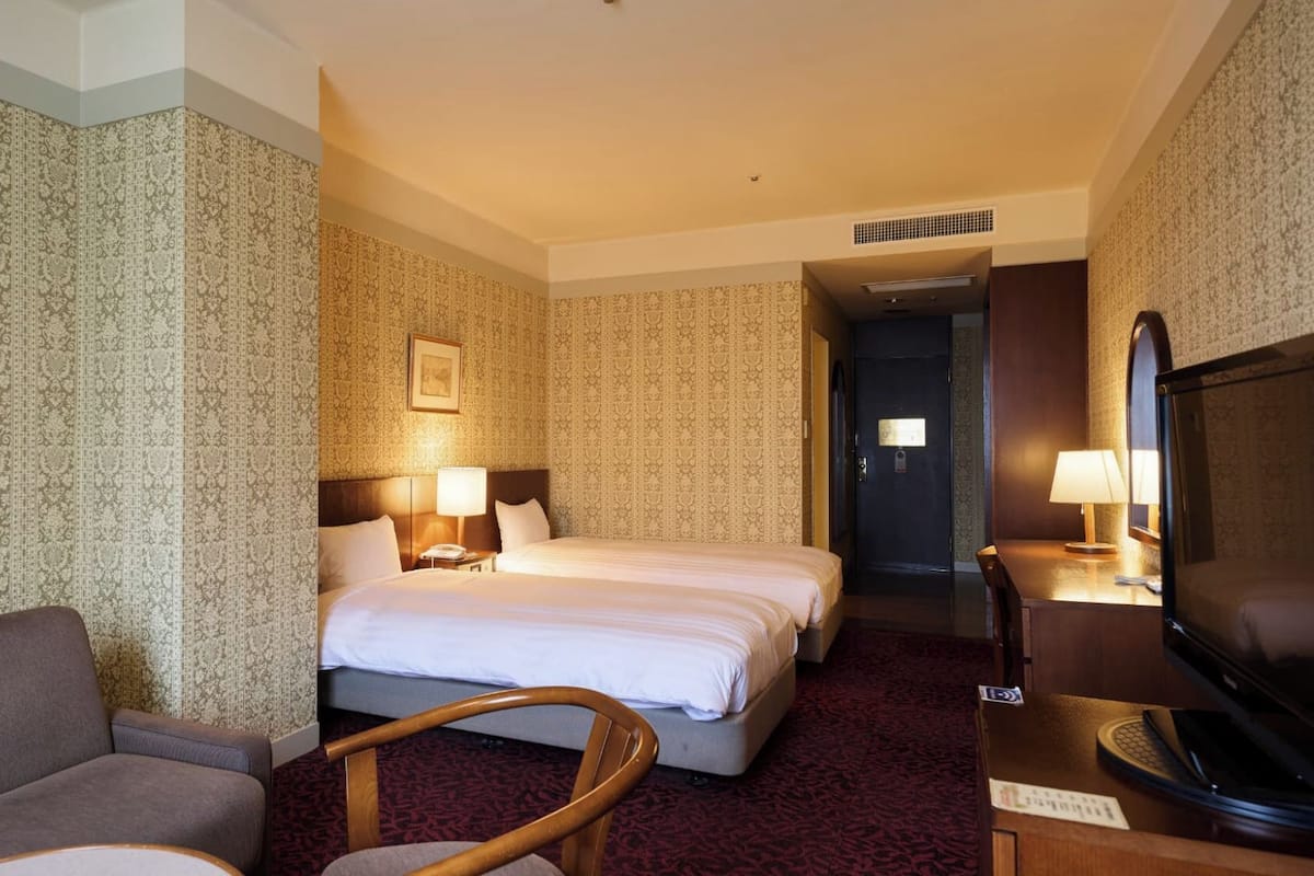 Ett hotellrum med två sängar, en soffa, en tv och ett skrivbord med en lampa.