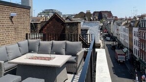 Une terrasse sur le toit, aménagée avec du mobilier d’extérieur, offrant une vue sur le paysage urbain et surmontée d’une grande antenne.