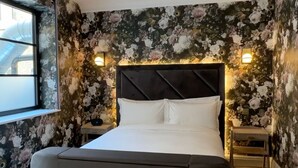 Une chambre moderne avec un grand lit, un lustre, un papier peint à motifs floraux et une fenêtre.