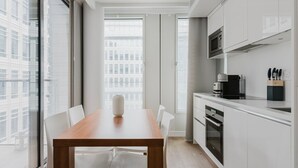 A modern kitchen with white cabinetry, a wooden dining table, and a view of the city through large windows.