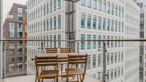 A balcony with a table and chairs, overlooking a modern building with a grid-like facade.