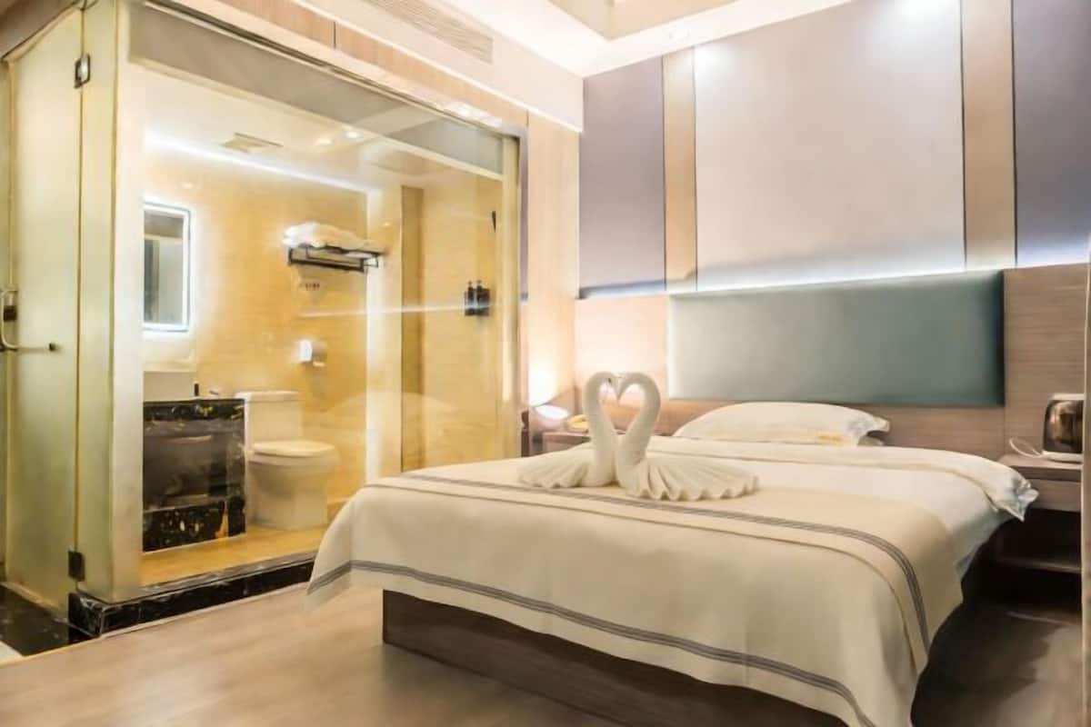 A hotel room with a bed, a glass-enclosed shower, and a bedside table.