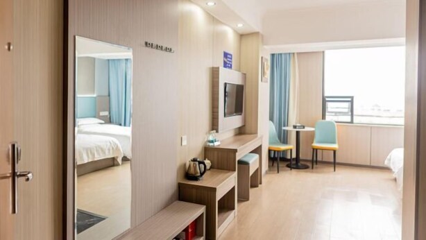 Een hotelkamer met een bed, een televisie, een bureau met stoel en een raam met gordijnen.