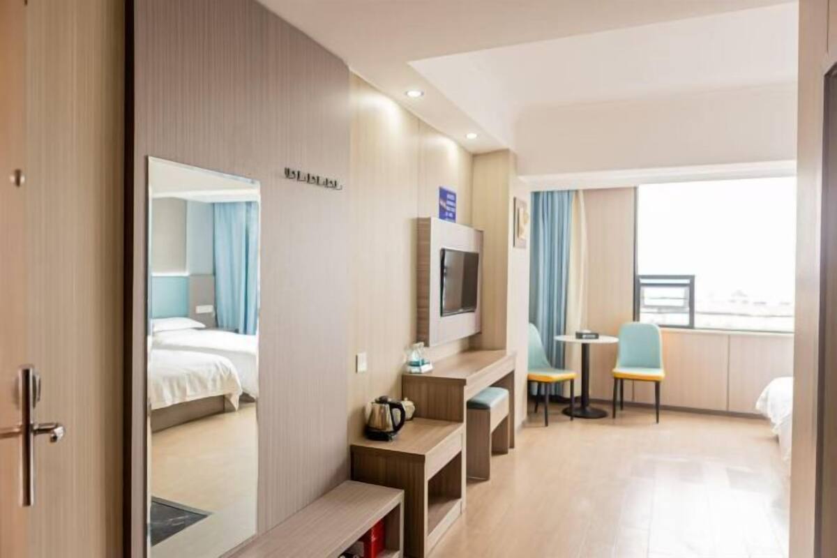 A hotel room with a bed, a TV, a desk with a chair, and a window with curtains.