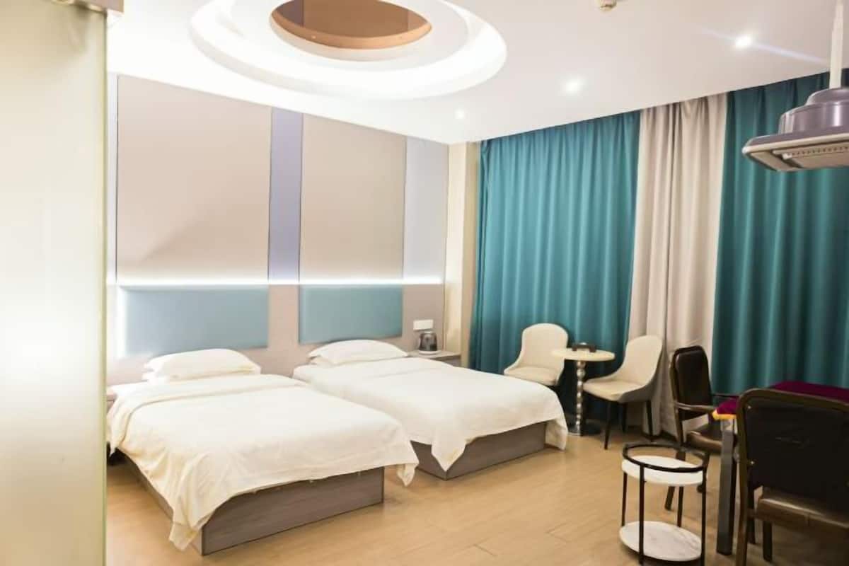 A hotel room with two beds, a desk, chairs, and a large window with curtains.