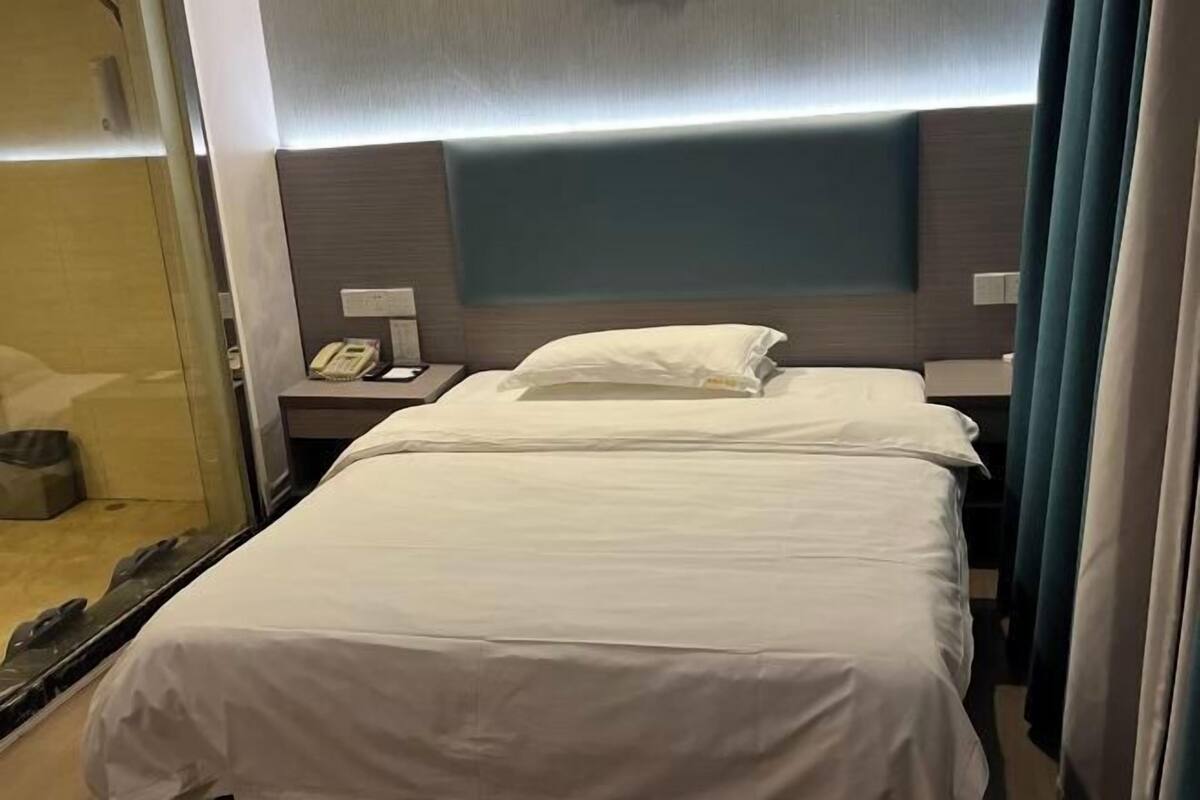 A hotel room with a bed, a bedside table with a phone, and a headboard.