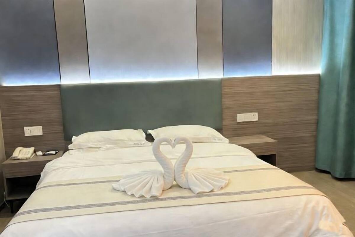 A hotel room with a bed, two nightstands, a phone, and a wall-mounted light fixture.