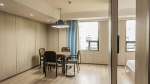 Een hotelkamer met een houten vloer, een eettafel met stoelen, een bed, een raam met gordijnen en een plafondlamp.