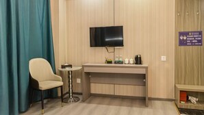 Een hotelkamer met een aan de muur bevestigde televisie, een klein rond tafeltje met een stoel, een houten bureau met een flatscreen-tv en een bordje aan de muur.