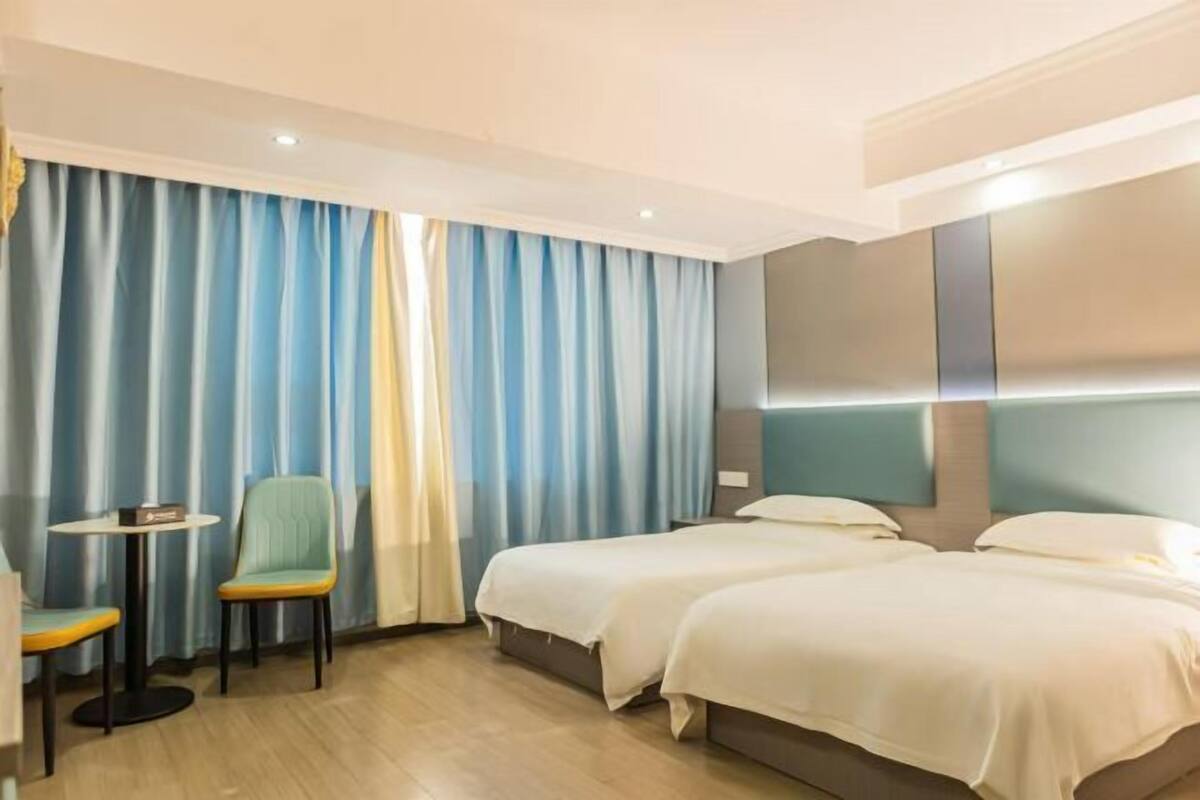 A hotel room with two beds, a small table, a chair, and a curtain.