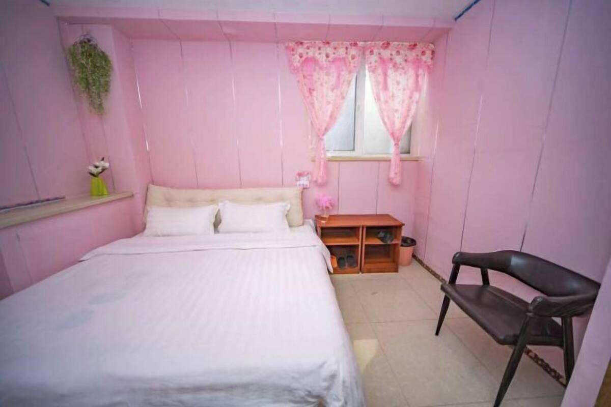 A bedroom with a bed, a chair, a window with curtains, a shelf with shoes, and a hanging plant.