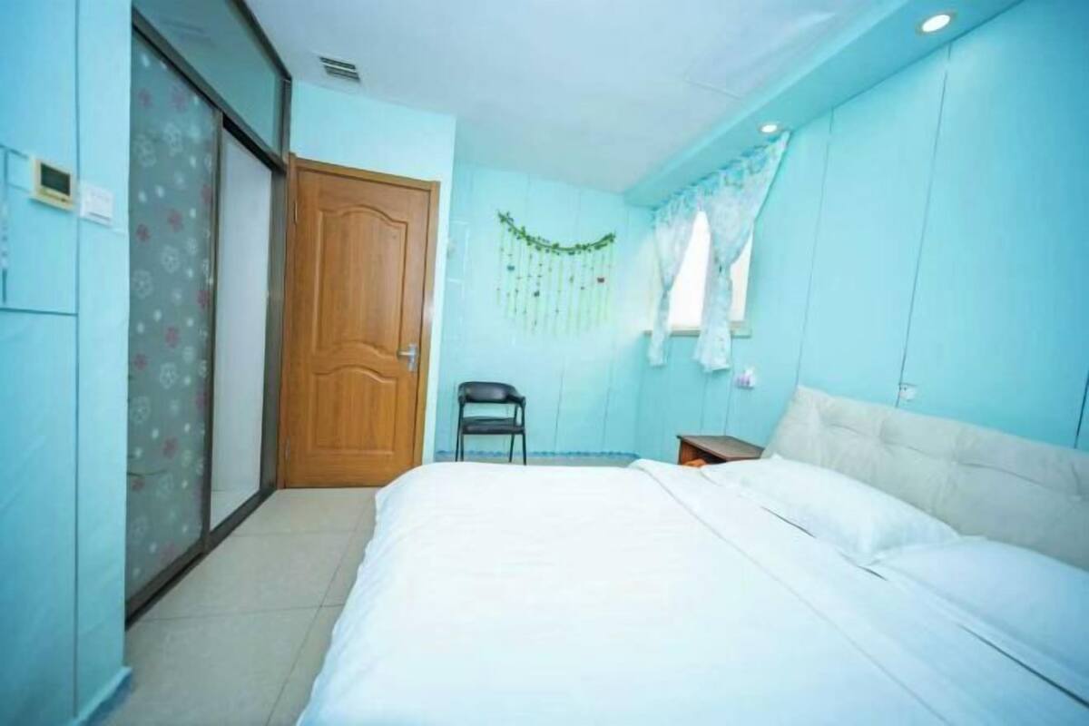 A bedroom with a bed, a chair, a wardrobe, and a door.