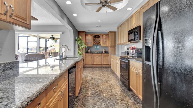 A modern kitchen with granite countertops, wooden cabinets, a black refrigerator, and a ceiling fan. - Pet Friendly Canal Front 3-Bedroom Grand Villa with Pool, Linai and Dock (Port Charlotte)