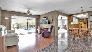 A spacious living area with a large window, a ceiling fan, and a dining area with wooden furniture. - Pet Friendly Canal Front 3-Bedroom Grand Villa with Pool, Linai and Dock (Port Charlotte)