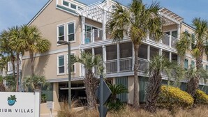 A multi-story building with balconies, palm trees, and a sign reading "Arium Villas".