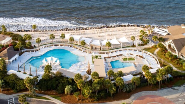 An aerial view of a resort with a large central pool, multiple smaller pools, and a beach area.