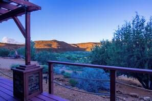 Una terraza de madera con chimenea de piedra, con vistas a un paisaje desértico de vegetación escasa y colinas distantes.