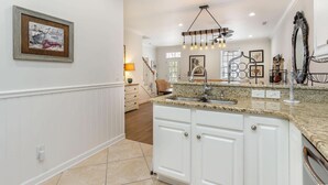 A kitchen with white cabinets, a granite countertop, a hanging light fixture, and a framed artwork on the wall. - Angler Villas 3 (Murrells Inlet)