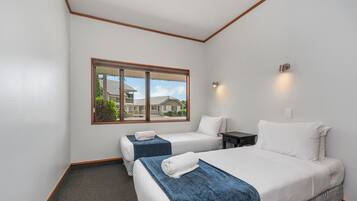 Habitación de hotel con dos camas, una ventana que da a vista de casas y una mesita con lámpara.