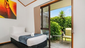 A hotel room with a bed, a painting, and a sliding glass door leading to a patio with a chair and plants. - Summit Motor Lodge (Tauranga)