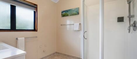 Un baño con cabina de ducha de vidrio, un lavamanos, un perchero para toallas y un cuadro en la pared.