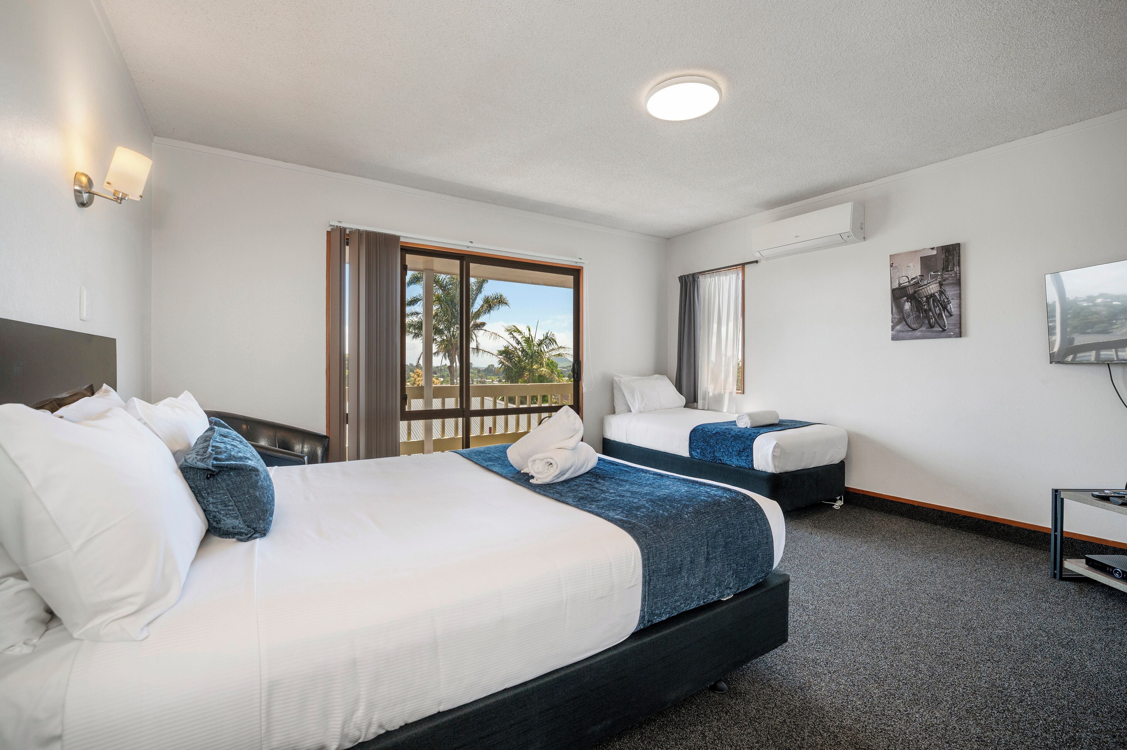 Habitación de hotel con dos camas, televisión y balcón con vistas.