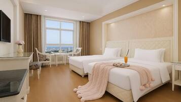 A hotel room with two beds, a desk, a chair, a TV, and a view of the city.