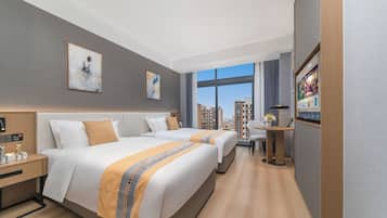 Ein Hotelzimmer mit zwei Betten, einem Schreibtisch, einem Sessel, einem Fernseher und Blick auf die Stadt.
