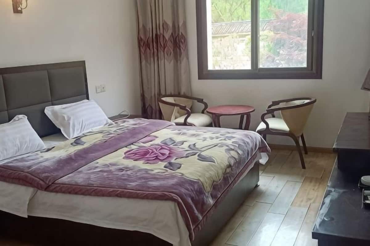 A hotel room with a bed, two chairs, a small table, and a window with a view.