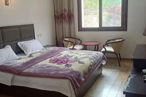 Hotellihuone, jossa on sänky, kaksi tuolia, pieni pöytä ja ikkuna, josta on näkymä.