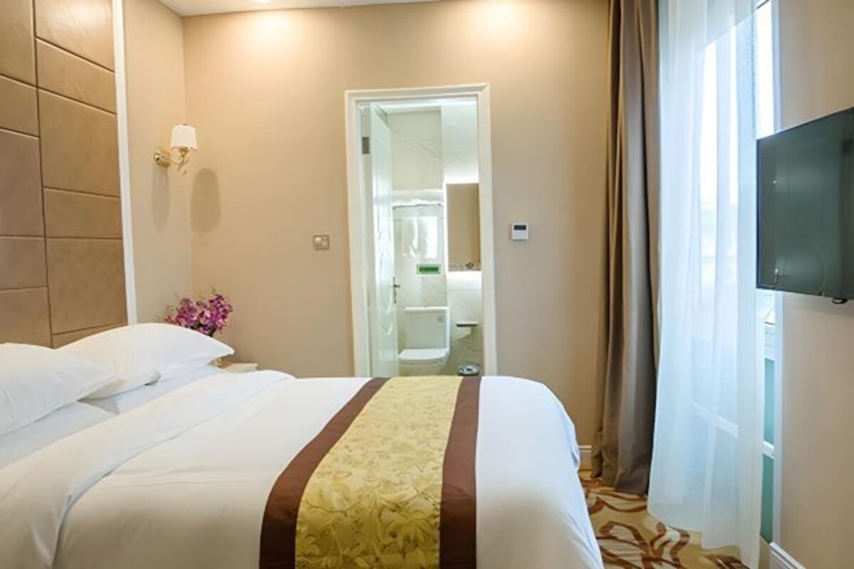 A hotel room with a bed, a television, a bathroom, and a view of the outdoors.