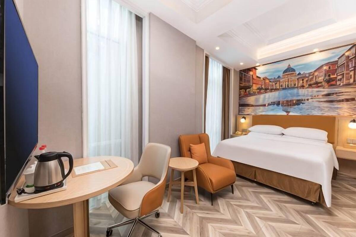 Une chambre d’hôtel avec un lit, un bureau doté d’une bouilloire, deux chaises, une petite table et une grande fenêtre.