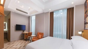 A hotel room with a large bed, a desk with a chair, a television, and a window with curtains. - Vienna Hotel (Suzhou)