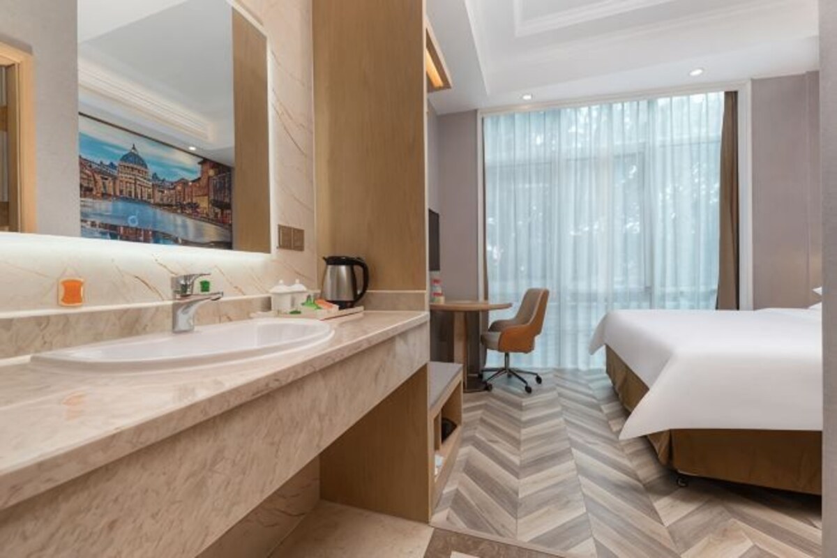 A hotel room with a large bed, a desk with a chair, a large mirror, and a bathroom with a sink and toilet.