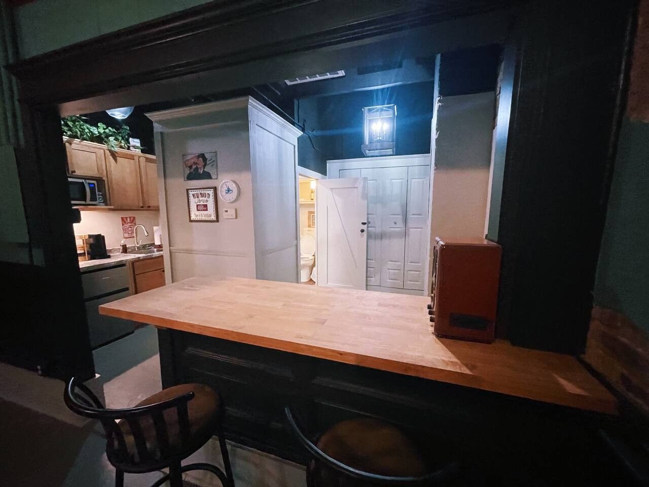 A compact kitchen with a wooden countertop, a microwave, and a refrigerator. There is a chair and a small table in the foreground.