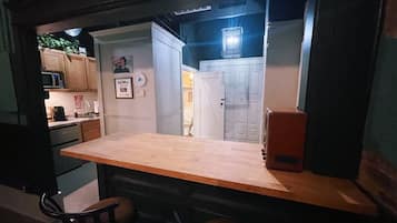 A compact kitchen with a wooden countertop, a microwave, and a refrigerator. There is a chair and a small table in the foreground.
