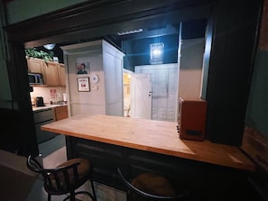 Cocina compacta con encimera de madera, microondas y refrigerador. Una silla y una mesa pequeña en primer plano.