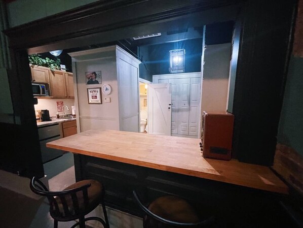 Cocina compacta con encimera de madera, microondas y refrigerador. Una silla y una mesa pequeña en primer plano.