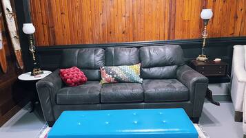 A room with a black leather sofa, a blue ottoman, and a wooden paneled wall.
