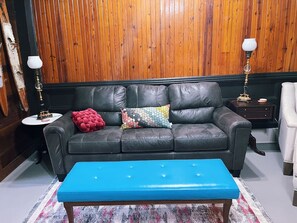 Una habitación con un sofá de cuero negro, un otomano azul y una pared revestida de madera.