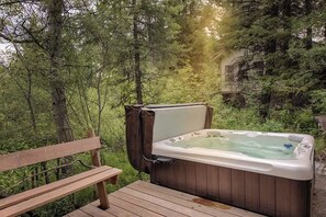 A hot tub in a forested area with a wooden bench and a building in the background.