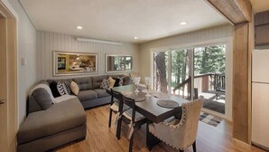 A cozy living area with a sofa, dining table, and chairs, a kitchen area with a window, and a deck with a railing. - Updated Cabin HotTub Firepit Decks nr Shore Lodge (McCall)