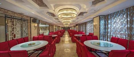 A hotel lobby with red chairs and tables, a chandelier, and a patterned wall.