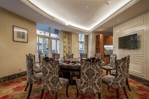 A dining area with a round table, patterned chairs, a flat-screen TV, and a view of the city.