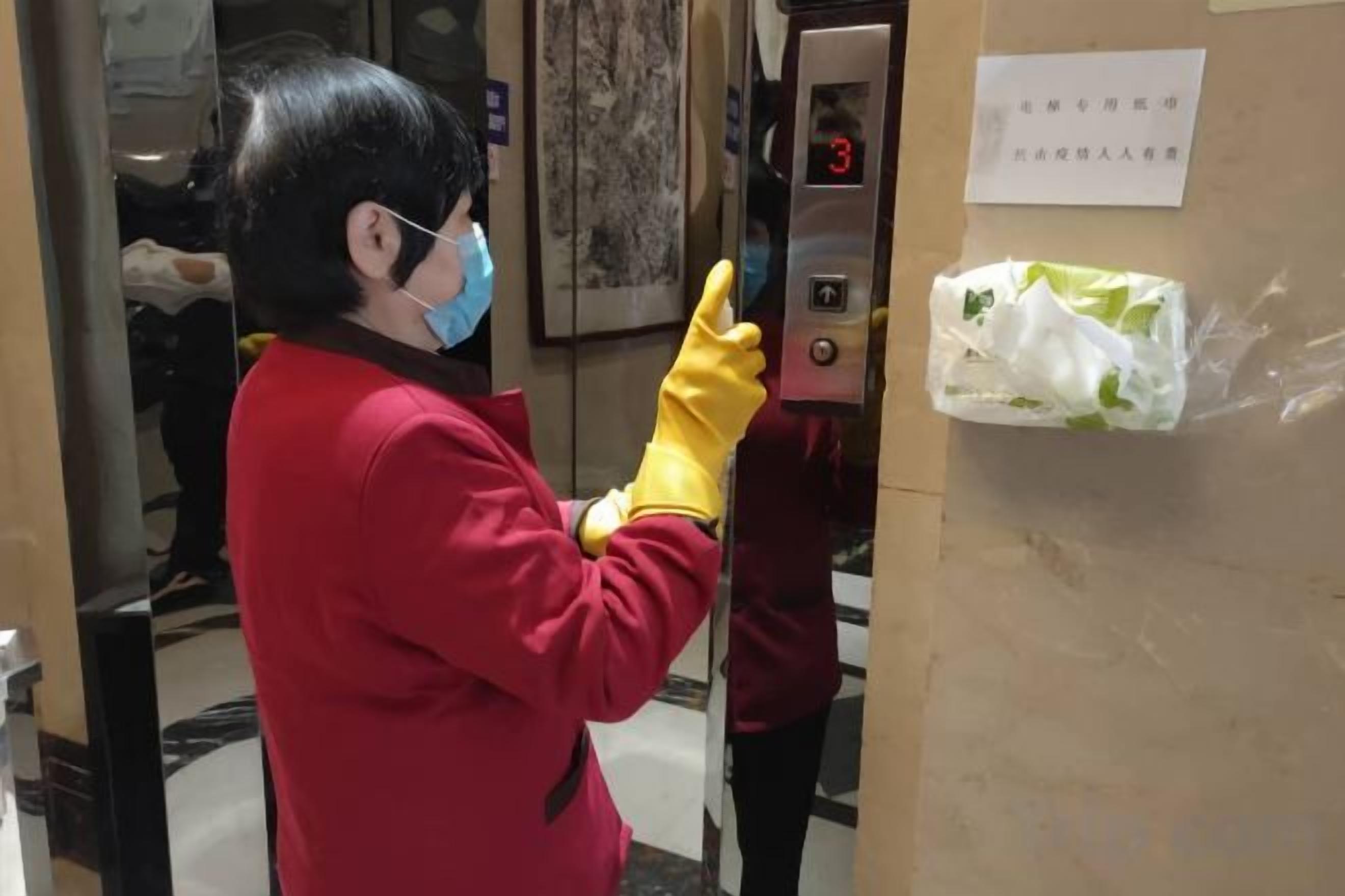 Una persona con una chaqueta roja y guantes amarillos interactúa con el panel de control de un ascensor.
