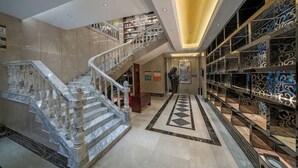 Eine prächtige Lobby mit einer Marmortreppe, einem zentralen Boden mit geometrischem Muster und einer Empore mit Bücherregalen.